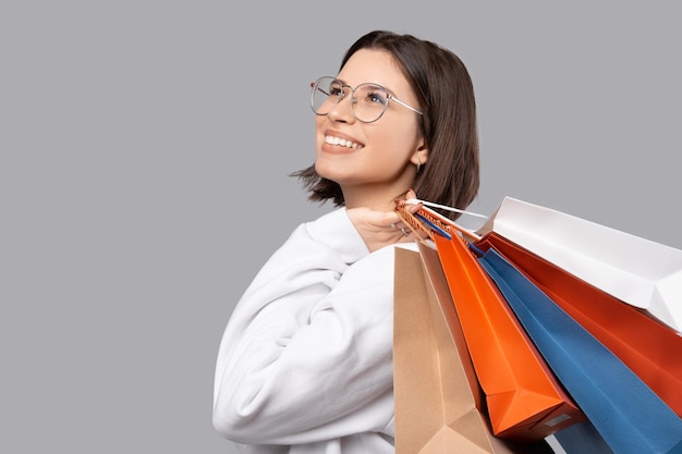 Czas na zakupy Zbliżenie na zdjęcie młodej modnej kobiety uśmiechającej się i trzymającej papierowe torby na zakupy na szarym tle