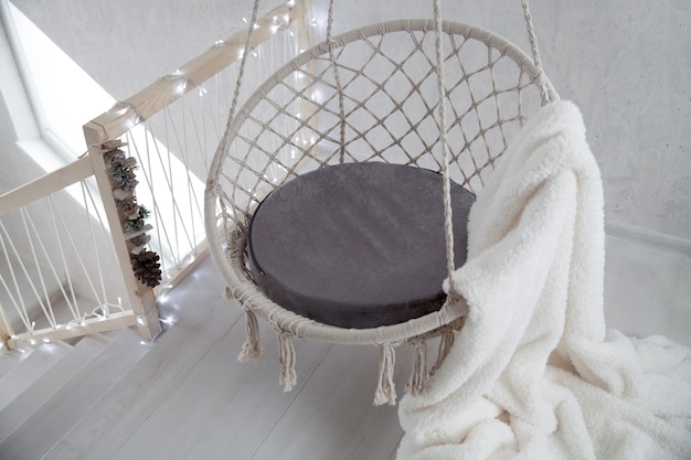 Czekając na Boże Narodzenie. Wiszące krzesło z białą, futrzaną kratą na tle pokoju ozdobionego girlandami