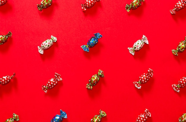 Czekoladki świąteczne umieszczone tworzące wzór na czerwonym tle na przemian czekoladki z czerwoną zieloną niebieską i białą opakowaniem