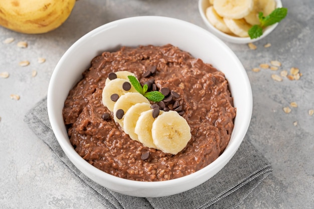 Czekoladowa owsianka z bananem i kawałkami czekolady na wierzchu w białej misce Zdrowe śniadanie