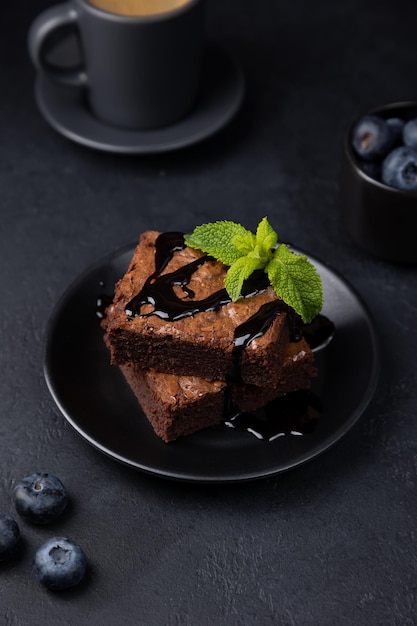 Czekoladowe ciasto brownie z miętowymi jagodami, polewą czekoladową i espresso Tradycyjny amerykański deser Popularne ciasto z ciemną czekoladą na czarnym tle Selektywne skupienie zbliżenia