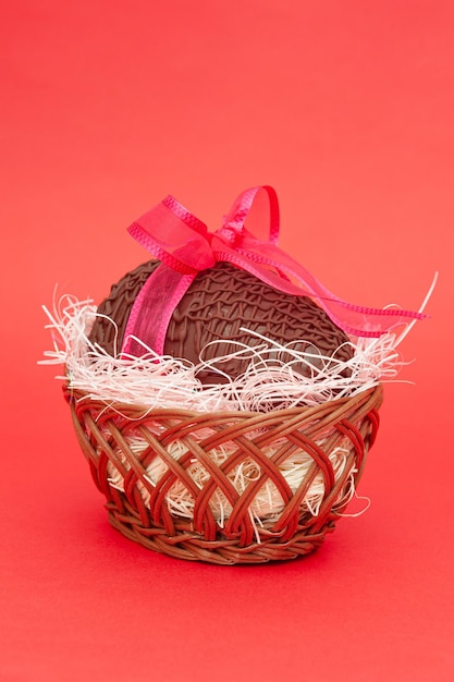 Czekoladowe jajko w pięknym wiklinowym koszu z czerwoną wstążką na prezent
