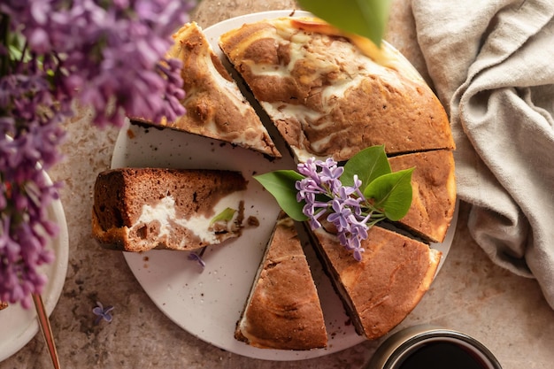 Zdjęcie czekoladowy sernik przekładany brownie i twarogiem ciasto czekoladowe pokrojone na brązowym teksturowanym tle z kwiatami bzu widok z góry w stylu rustykalnym