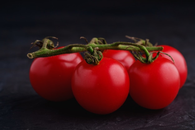 Czereśniowego pomidoru gałąź, świezi dojrzali organicznie warzywa na ciemnej czerni powierzchni, makro- kąta widok