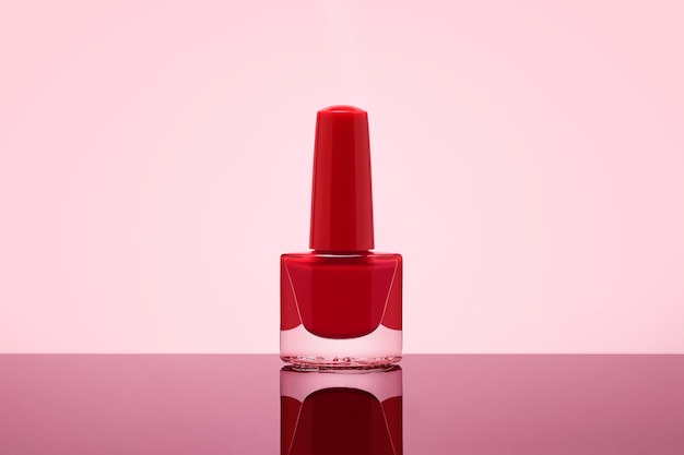 Czerwona butelka lakieru do paznokci na pastelowym różowym tle