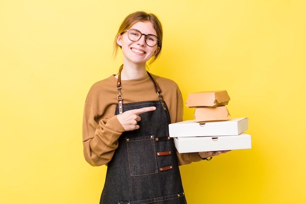 Czerwona głowa ładna kobieta uśmiecha się radośnie czując się szczęśliwa i wskazując na bok fast food zabiera delikatną