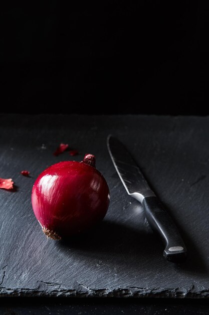 Zdjęcie czerwona hiszpańska cebula z nożem kuchennym na tle łupkowym