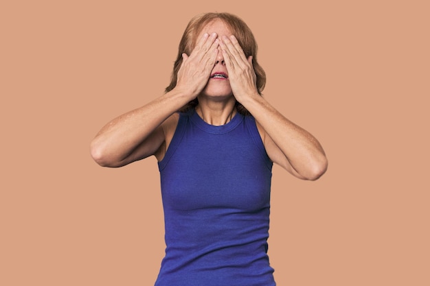 Zdjęcie czerwona kobieta w średnim wieku w studiu, boi się zakrywać oczy rękami.