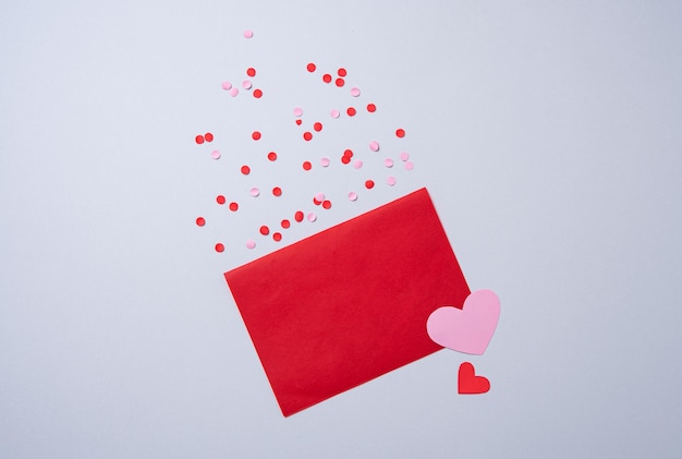 Czerwona papierowa koperta z wolnym miejscem na tekst z sercami i konfetti na szarym tle. Pojęcie Walentynek. Płaski świecki, widok z góry.