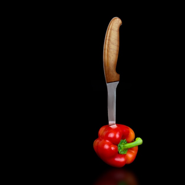 Czerwona papryka z nożem szefa kuchni na czarnym tle
