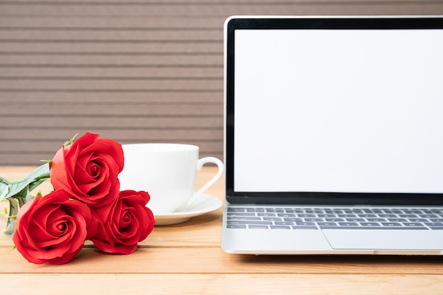Czerwona róża i filiżanka kawy z makieta laptopa na tle drewna, koncepcja Valentine