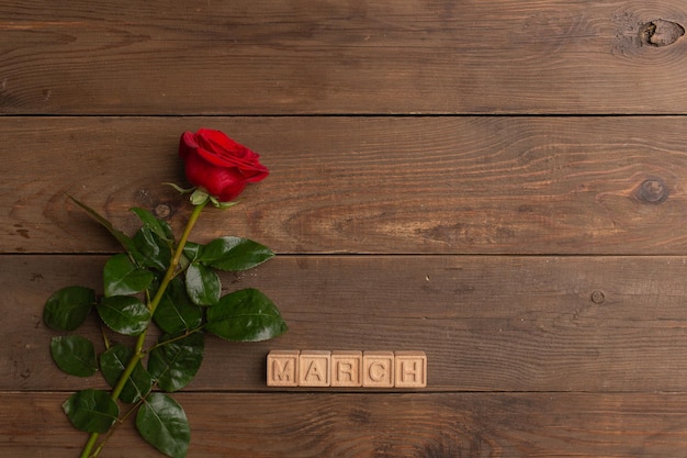 Czerwona róża z napisem marca na drewnianych kostkach na drewnianym tle
