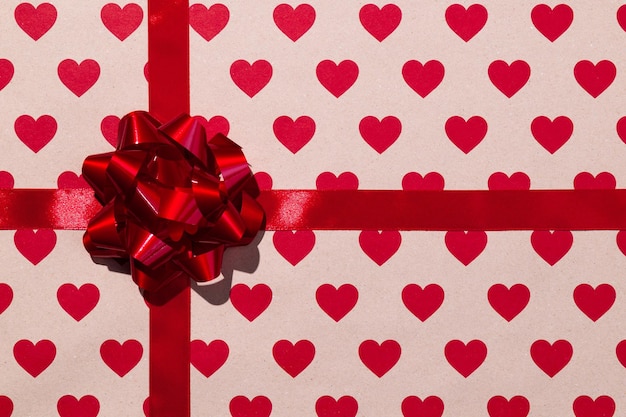 Czerwona wstążka na prezent i kokarda na tle papieru rzemieślniczego z sercami