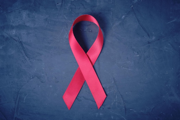 Czerwona wstążka na tle tekstury betonu, symbol choroby Aids i problem nadużywania narkotyków.