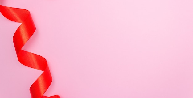 Zdjęcie czerwona wstążka satynowa z boku na różowym tle