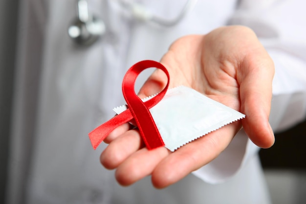 Zdjęcie czerwona wstążka symbolizująca pomoce i prezerwatywy w rękach lekarza w białym fartuchu