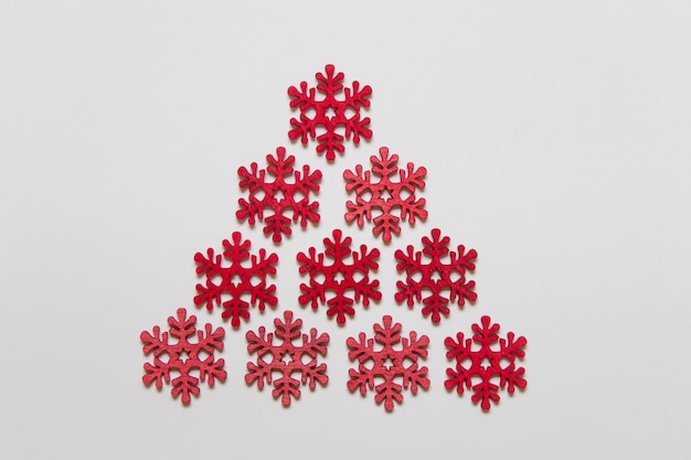 Czerwone drewniane płatki śniegu ułożone w trójkąt na białej powierzchni