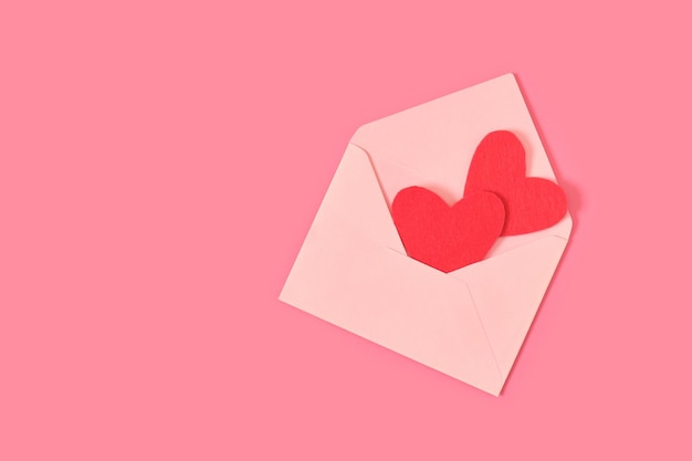 Czerwone filcowe serca w jasnej papierowej kopercie na różowym tle