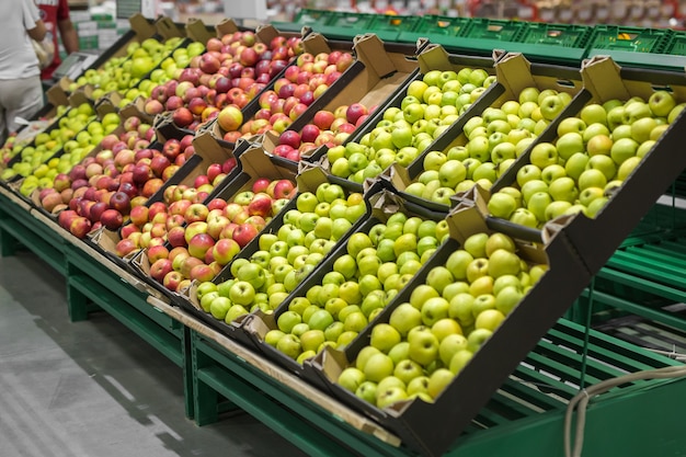 Czerwone i zielone jabłka na ladzie rynku. Jabłka w kartonach na półce w sklepie spożywczym.