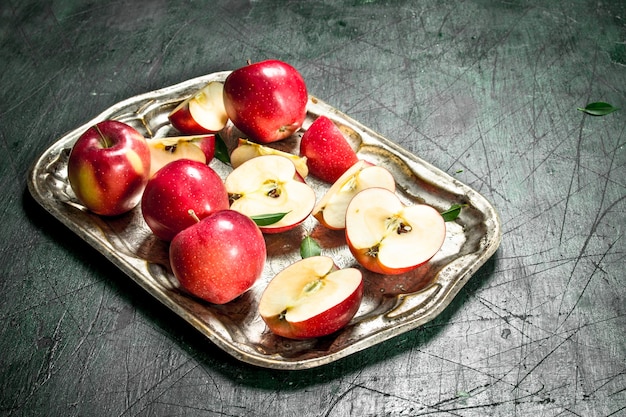 Czerwone jabłka na stalowej tacy z liśćmi na rustykalnym stole.