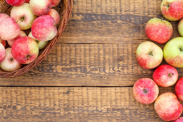 Czerwone jabłka w wiklinowym koszu i na starych drewnianych deskach z ogrodowymi rękawiczkami. Widok z góry z miejscem na kopię