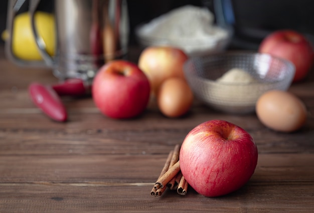 Czerwone jabłko z cynamonem i składnikami do gotowania szarlotki na ciemnobrązowym tle