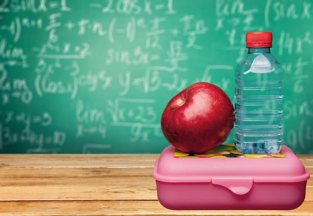 Czerwone jabłko z wodą i jedzeniem na szkolnej ławce