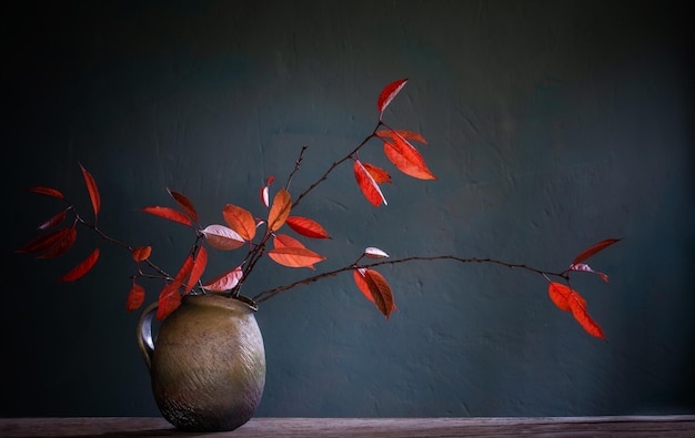 Czerwone jesienne liście w ceramicznym dzbanku na starym drewnianym stole