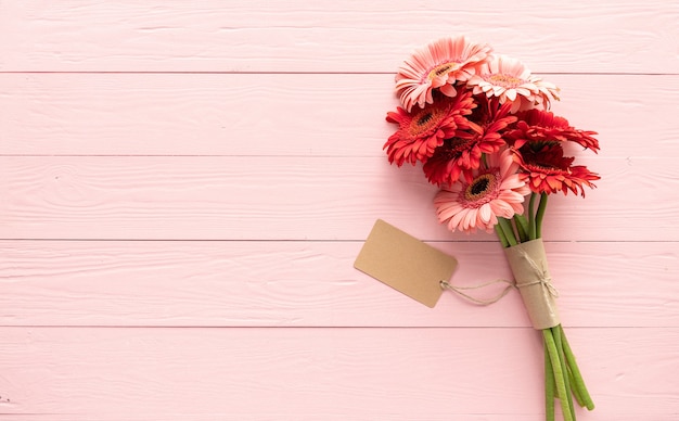Czerwone kwiaty stokrotki gerbery i pusta etykieta rzemieślnicza na różowym drewnianym stole, płaskie lay