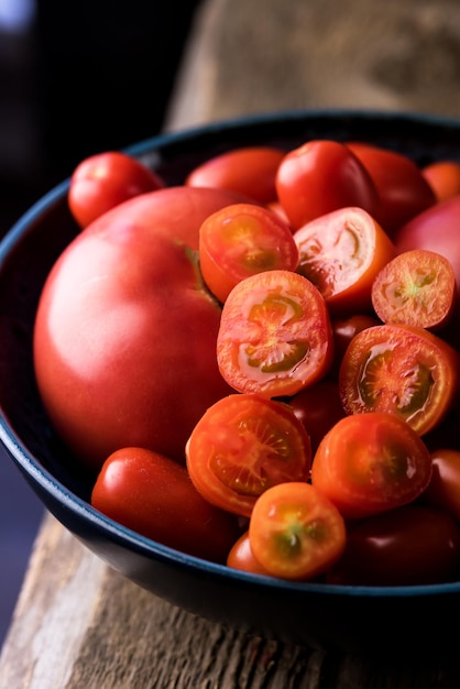 Zdjęcie czerwone małe i duże pomidory na niebieskim talerzu na drewnianym tle organiczne warzywa pionowe