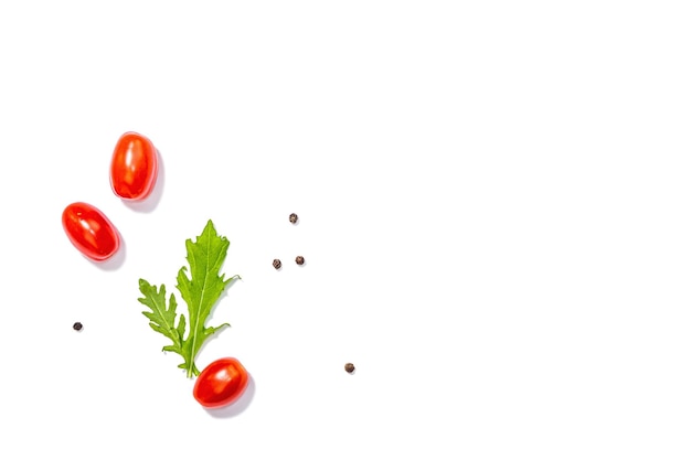 Czerwone pomidory wiśniowe z arugulą i pieprzem na białym tle