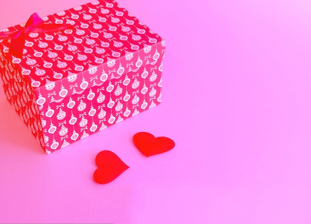 Zdjęcie czerwone pudełko przewiązane czerwoną wstążką na modnej różowej powierzchni