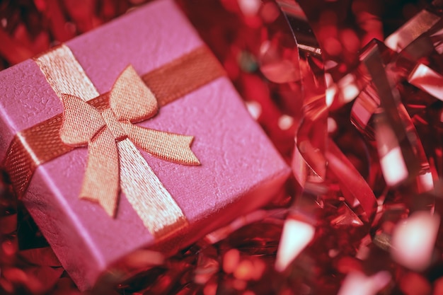 Czerwone pudełko w świątecznym świecidełku. Małe zamknięte pudełko z kokardą i prezentem