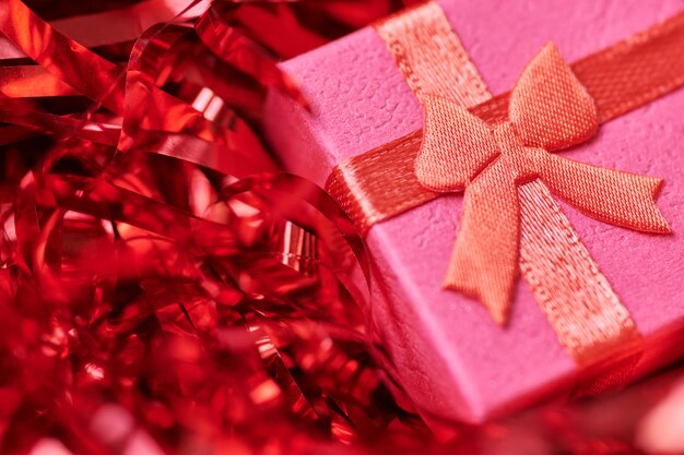 Czerwone pudełko w świątecznym świecidełku. Małe zamknięte pudełko z kokardką i prezentem na rocznicę lub ślub. Pudełko z niespodzianką dla ukochanej osoby.