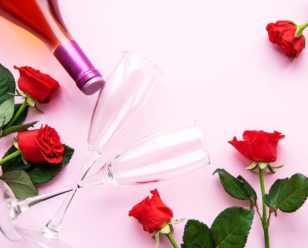 Czerwone róże, wino i kieliszki do wina na jasnym różu