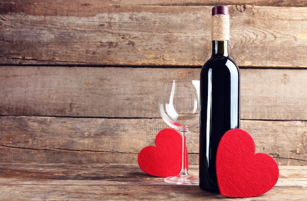 Czerwone serca z butelką wina i kieliszkami na drewnianym tle