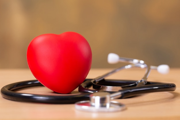 Czerwone serce i stetoskop na drewnianym stole.