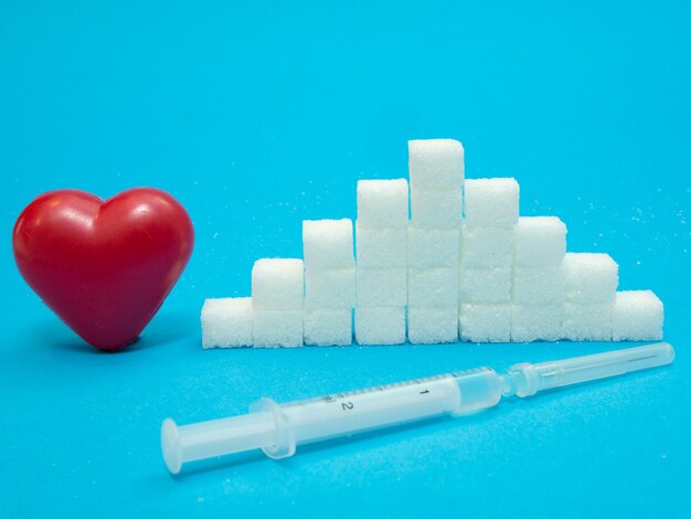 Czerwone Serce, Stos Białych Kostek Cukru Rafinowanego I Strzykawka Z Insuliną Na Niebieskim Tle