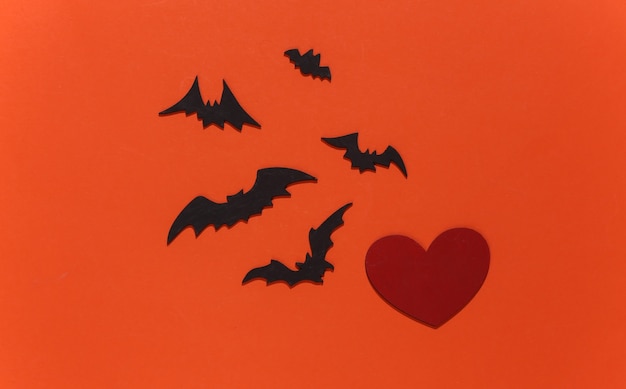 Czerwone serce z nietoperzami i pająkami na pomarańczowym jasnym tle. Motyw Halloween.
