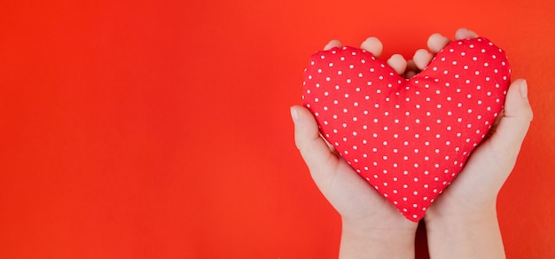 Zdjęcie czerwone serce z tkaniny w dłoniach na czerwonym tle