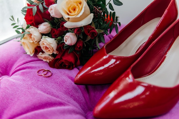 Zdjęcie czerwone skórzane buty panny młodej w pobliżu złotych pierścieni ślubnych i bukiet róż