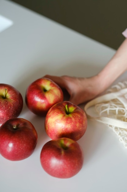 Zdjęcie czerwone słodkie jabłka w siateczkowej ekologicznej torbie na białym stole zakupy na rynku i zero waste