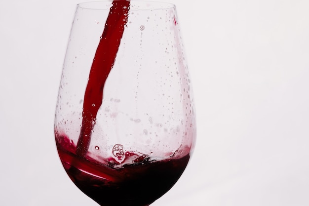 Czerwone wino rozpryskiwania się w szklance. Kieliszek wina na białym tle.