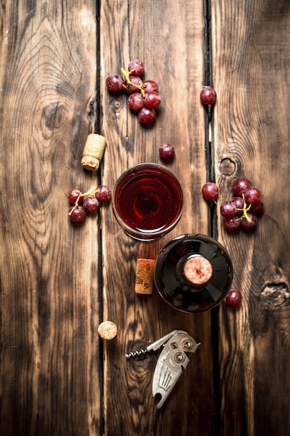 Czerwone wino z gałązką winogron i korkociągiem. Na drewnianym stole.