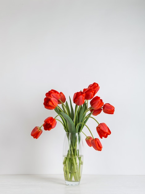 Czerwoni tulipany w wazie na stole na bielu