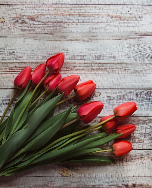 Czerwoni tulipany z liśćmi kłamają na drewnianym tle