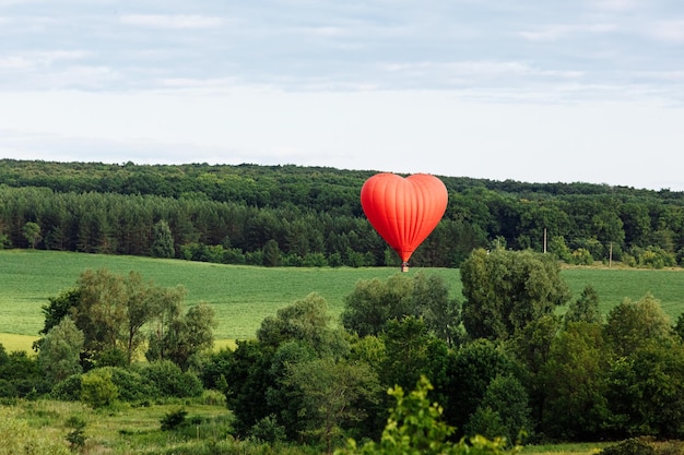 Czerwony balon na ogrzane powietrze w kształcie serca ląduje na zielonym polu