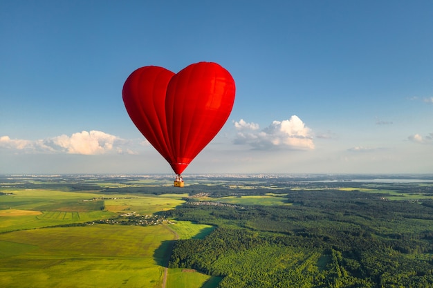 Czerwony balon w kształcie serca z ludźmi nad zielonymi polami i lasami.