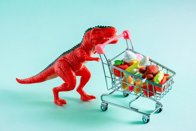 Czerwony dinozaur z koszykiem pełnym żywności na niebieskim tle Koncepcja zakupów żywności