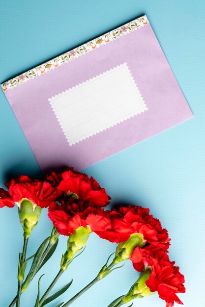 Czerwony goździk i różowa papierowa koperta z miejscem na tekst na niebieskim tle widok z góry